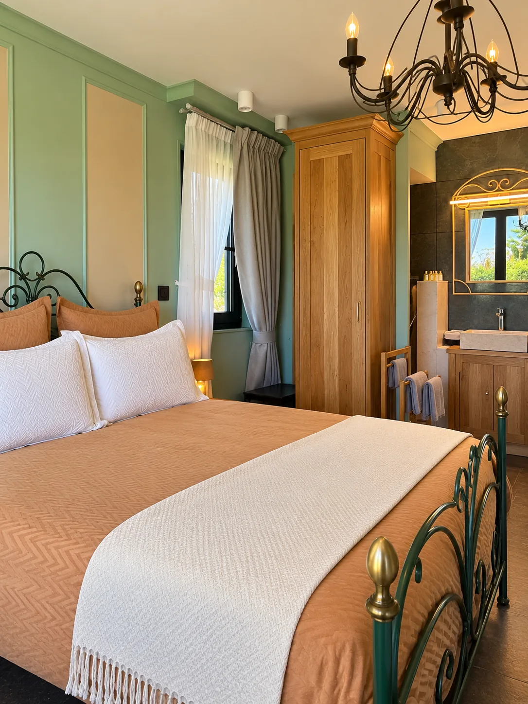 Chambre Double Deluxe aux murs vert sauge, lit en fer forgé et salle de bains visible en arrière-plan