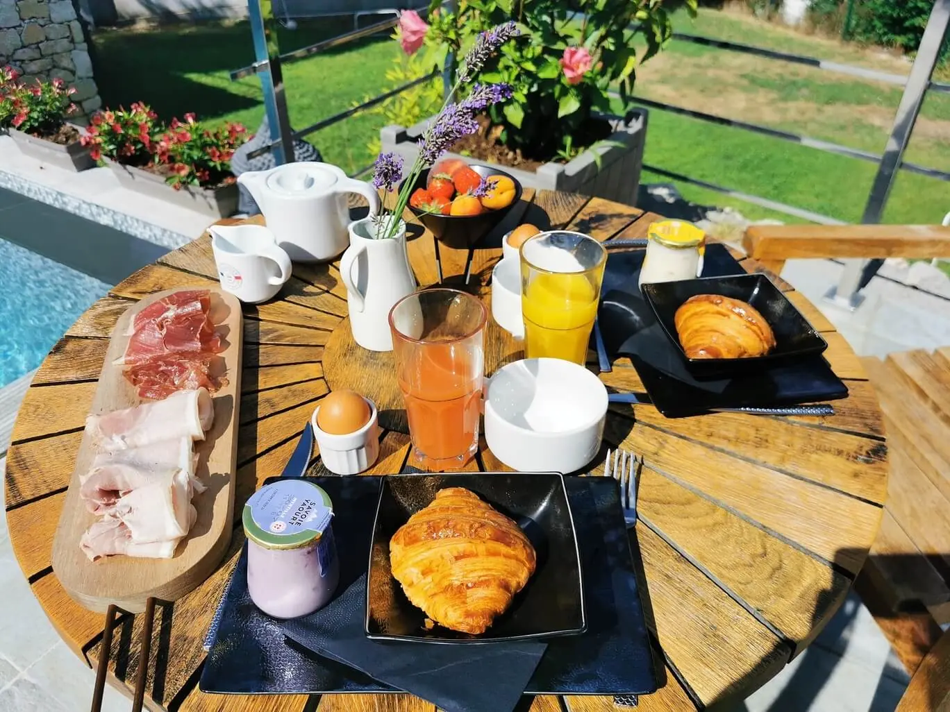 Petit-déjeuner servi en terrasse au bord de la piscine, avec viennoiseries, jus frais et charcuterie