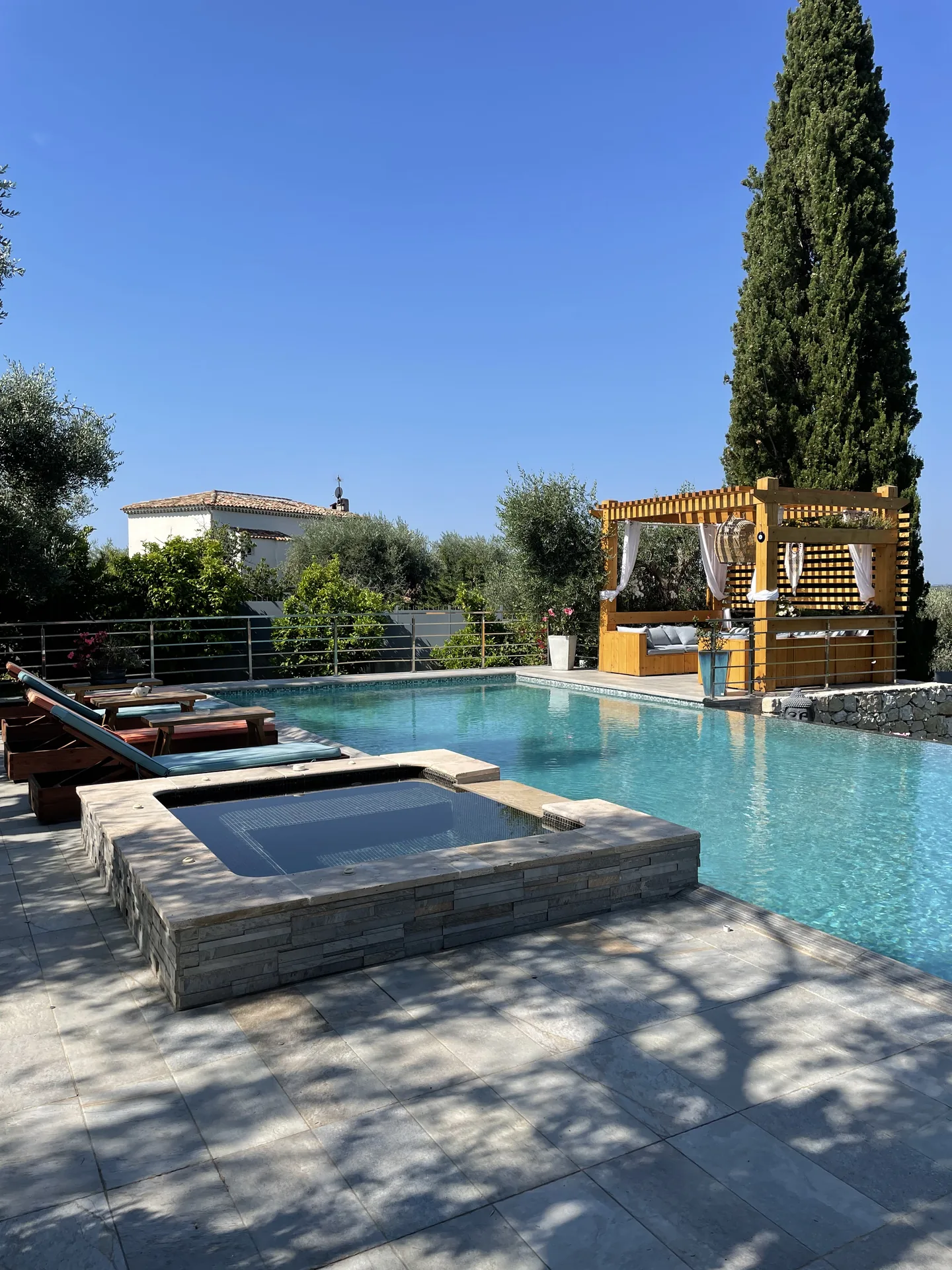 Jacuzzi en pierre et pergola en bois au bord de la piscine, sous un cyprès