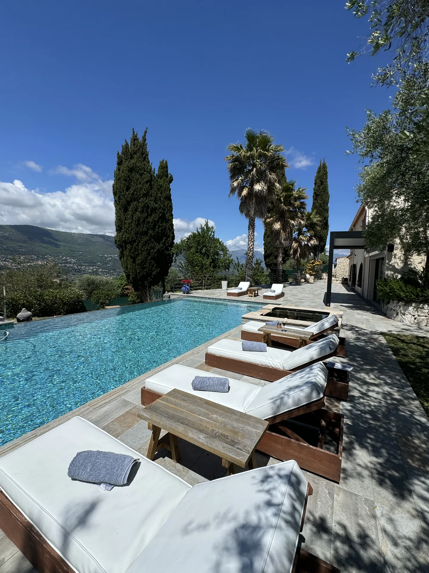 Piscine bleue bordée de transats blancs, avec vue sur les collines de Nice