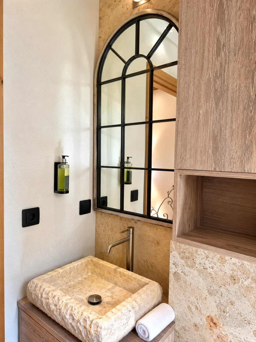 Lavabo en pierre sous un miroir cintré à croisillons noirs dans la Suite Deluxe